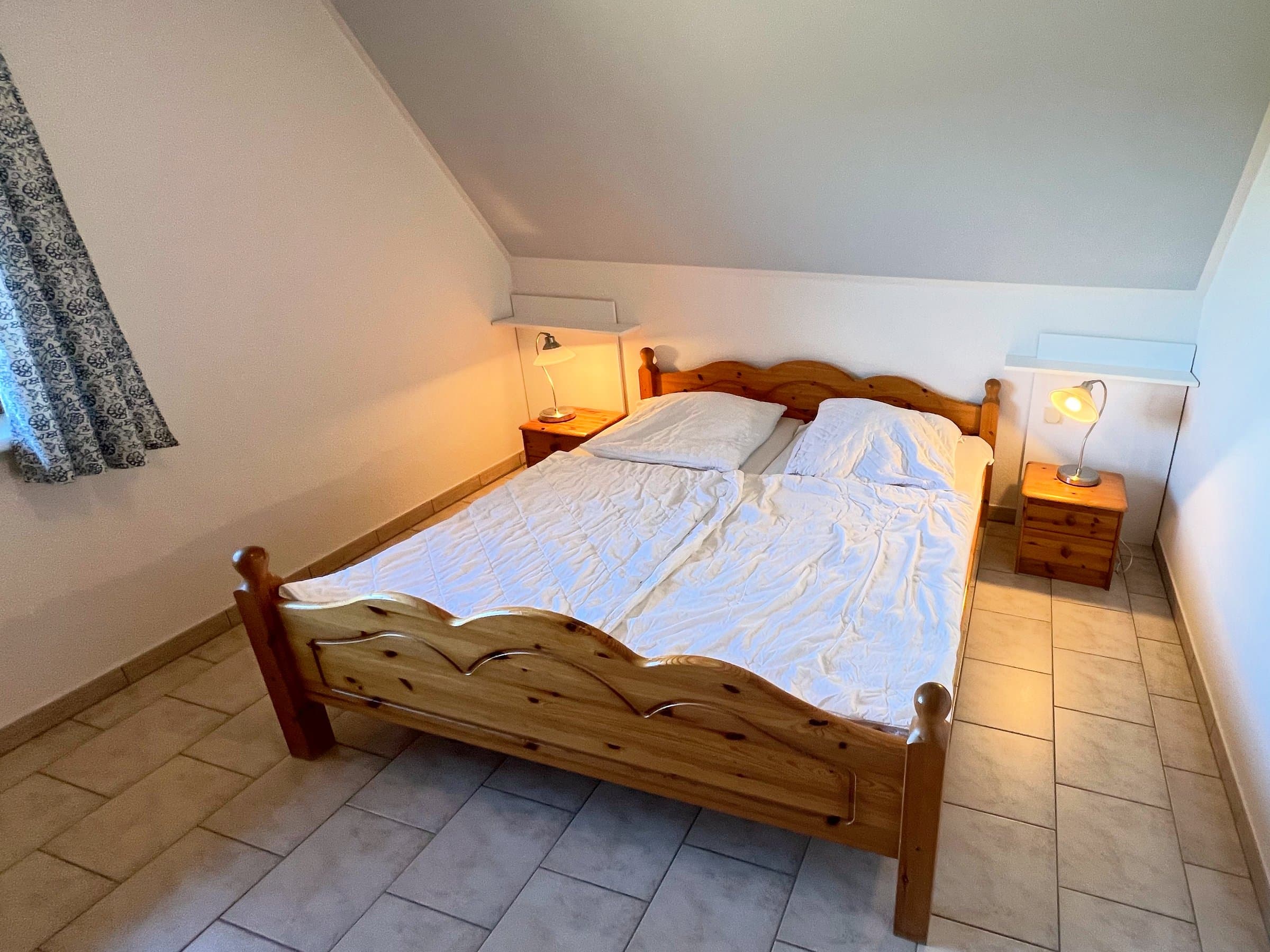 Doppelbett aus Holz mit zwei Nachttischen und Leselampen unter der Dachschräge
