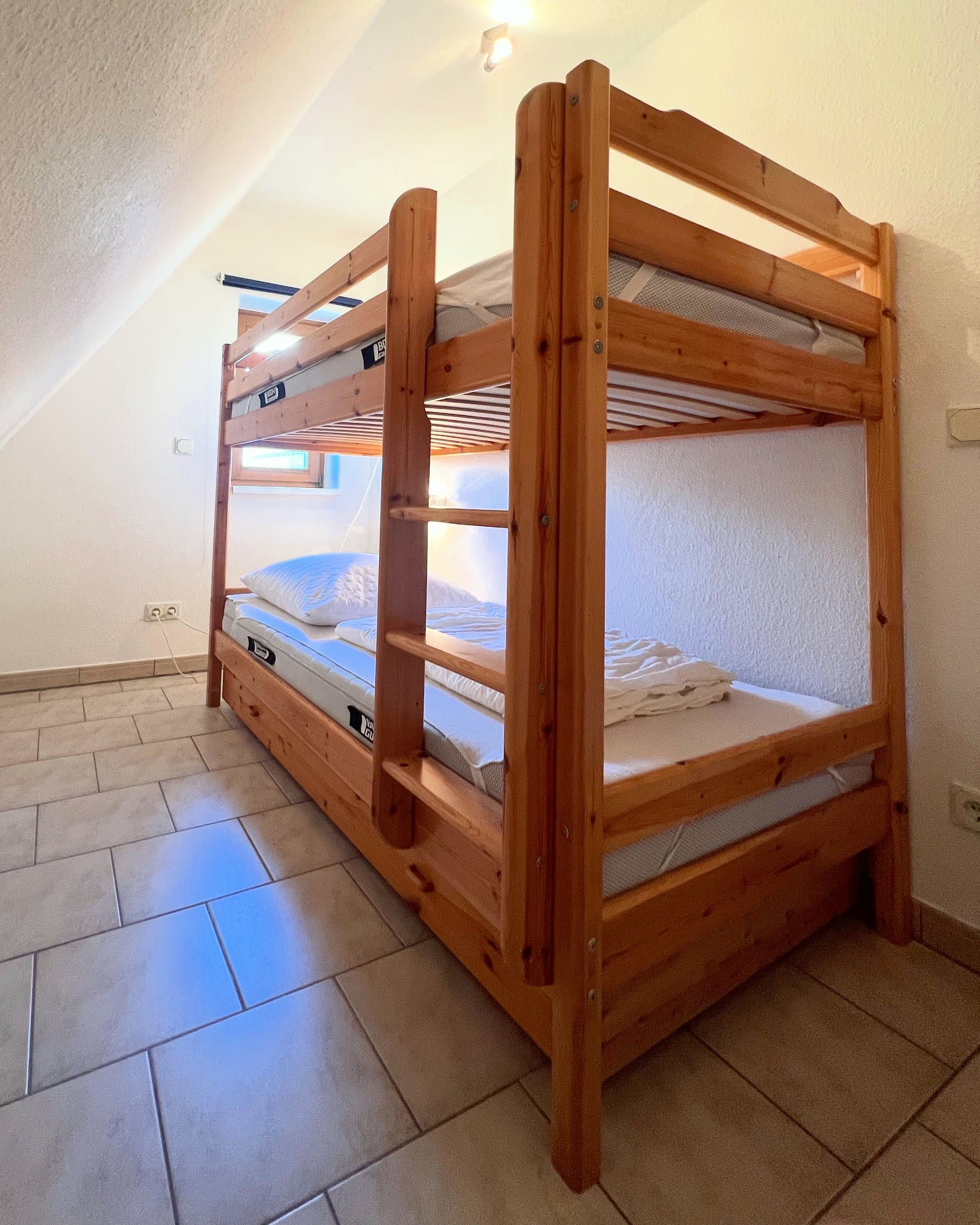 Etagenbett aus Holz mit Leiter in einem schmalen Zimmer unter der Dachschräge